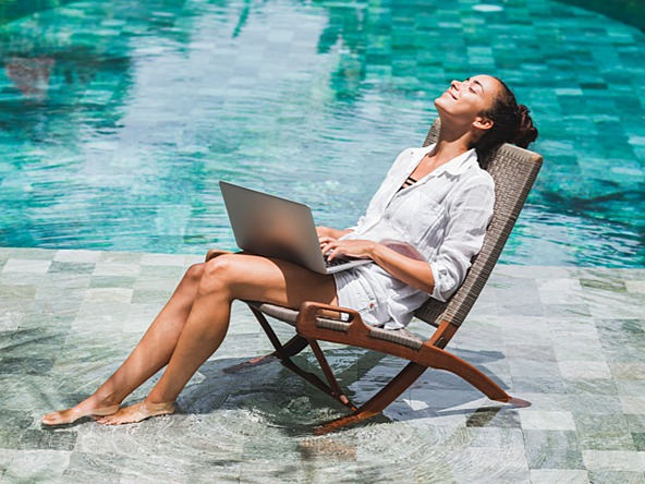 Woman sunning herself by the pool while working on a laptop